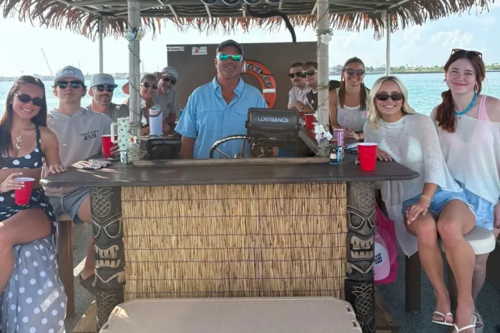 Group of people with drinks on a tiki bar boat on the water.