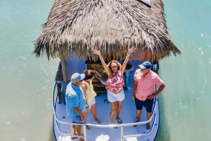 Four people on a small, thatched-roof boat, with one woman raising her arms.