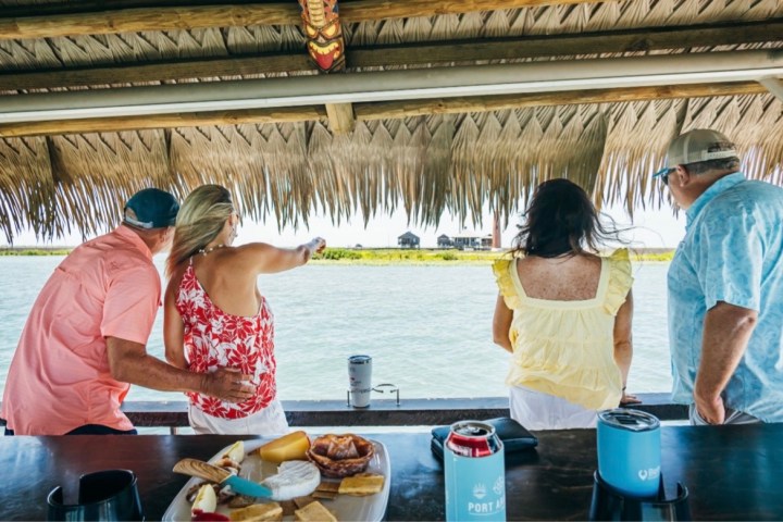 Four people on a tiki boat overlook the water with snacks on the counter.