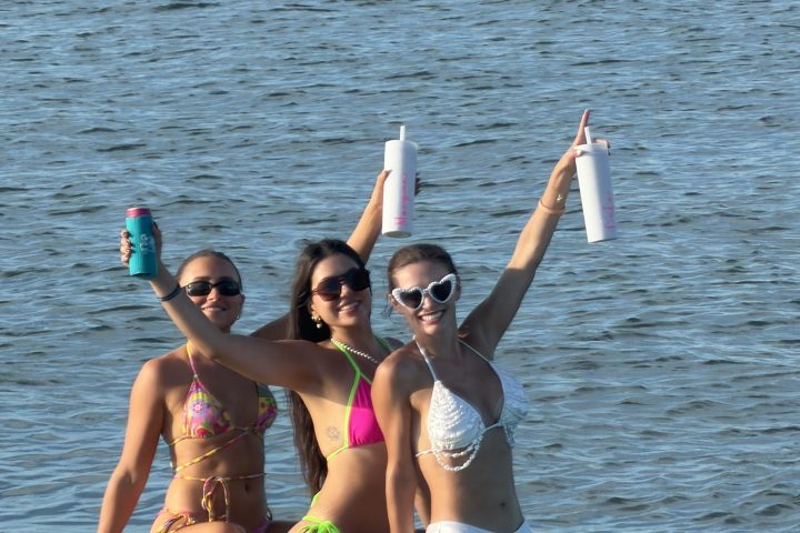 Three people sitting on paddleboards in swimsuits, holding bottles, on a calm body of water.