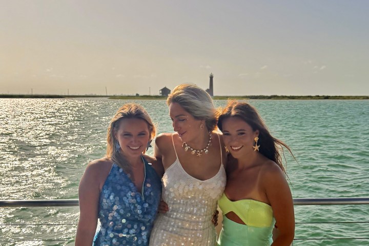Three people posing on a boat with ocean and lighthouse in the background.
