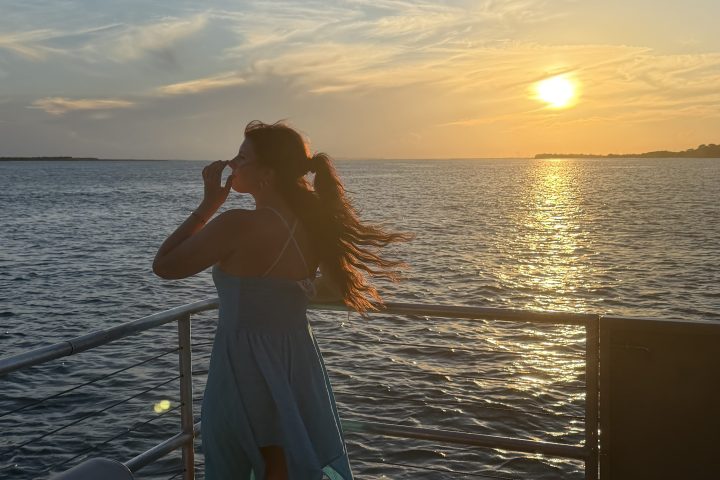 Woman in a dress on a balcony overlooking the ocean at sunset.