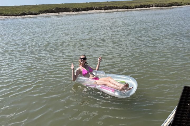 Person floating on an inflatable in a lake, surrounded by a thatched roof and blue sky.