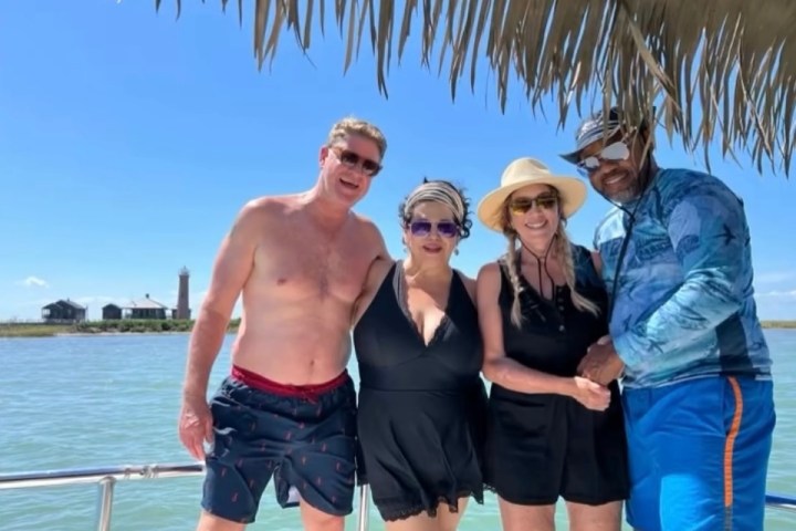 Four people posing on a boat near water under sunny skies.