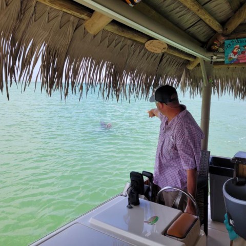 Person on a boat pointing at water under a thatched roof.