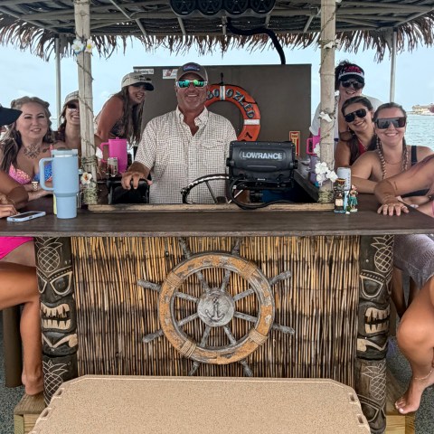 Group of people at a tiki bar on a boat, smiling and posing for a photo.