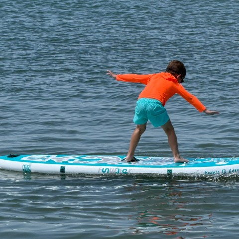 Child balancing on a paddleboard in a large body of water.