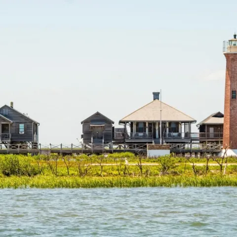 Lighthouse and rustic buildings by the water on a sunny day.